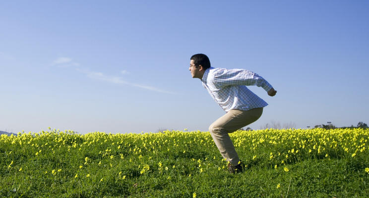 A man bracing himself to jump into the air amidst a field of vibrant yellow flowers, capturing a moment of freedom, energy, and joyful exuberance