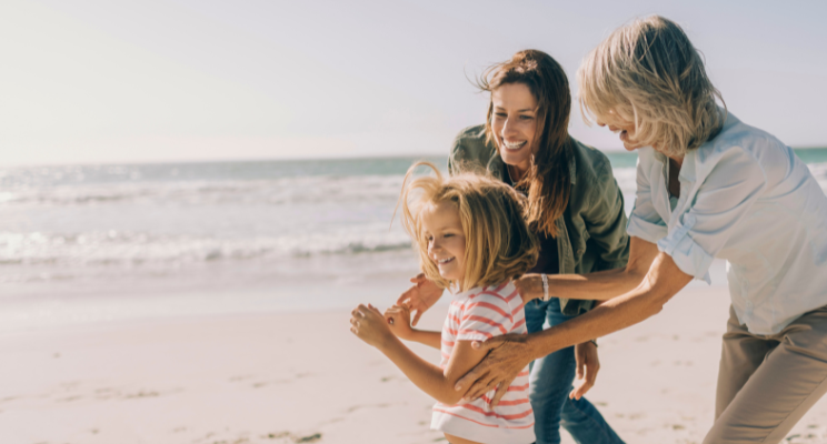 A multigenerational group of women, including a little girl, playing and smiling together on a beach, radiating joy, connection, and cherished family moments.